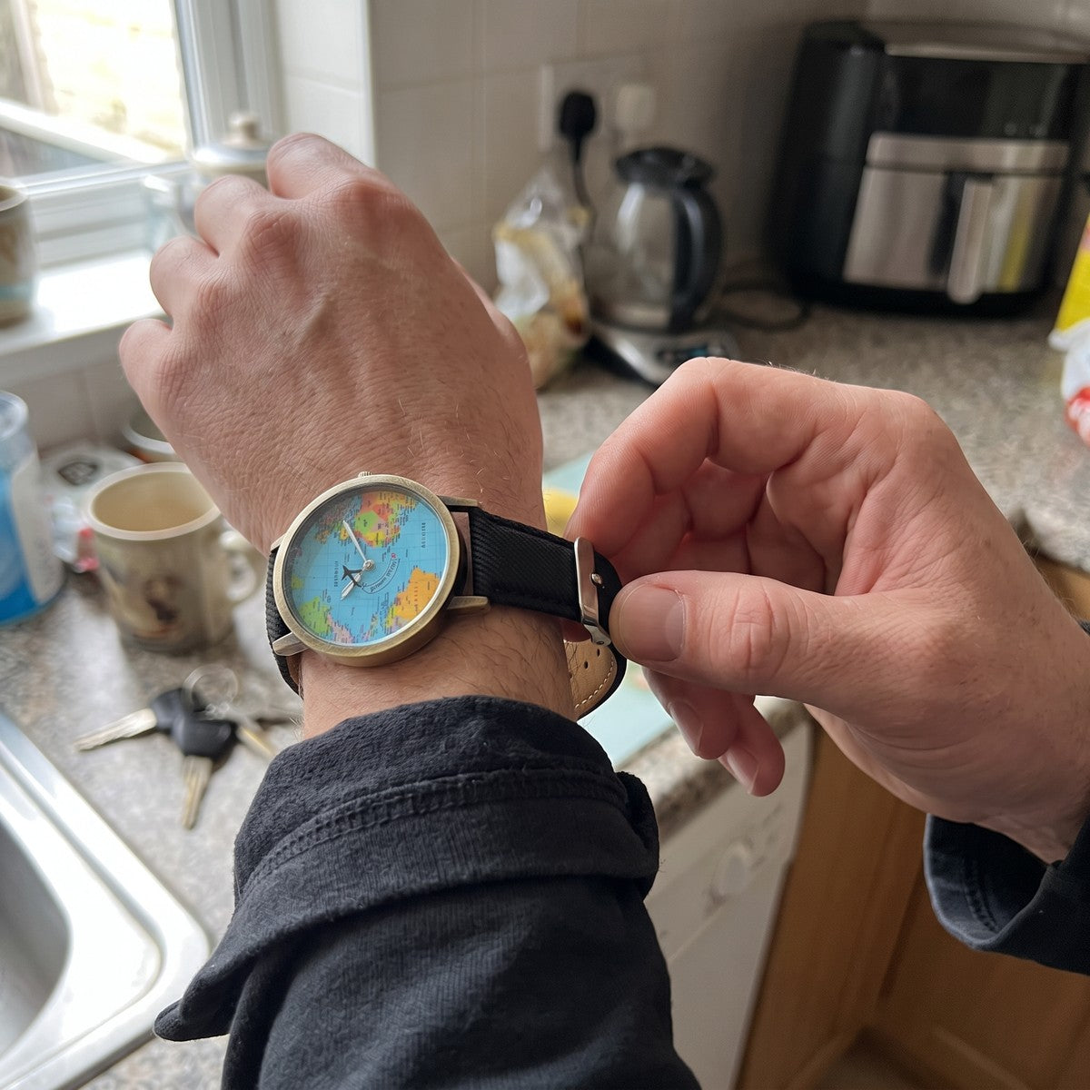 Hands fastening a Black Skybound watch in a kitchen