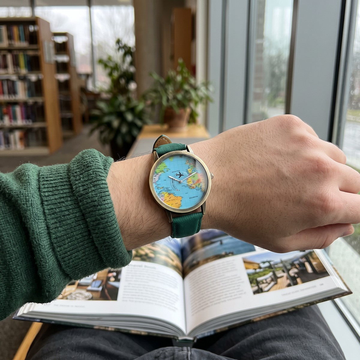 Green Skybound watch on a wrist beside a library book